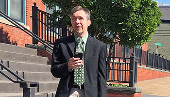 A man standing outside listens to NFB-NEWSLINE on his mobile phone.