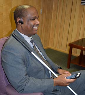 A man smiles while listening to NFB-NEWSLINE on his phone.